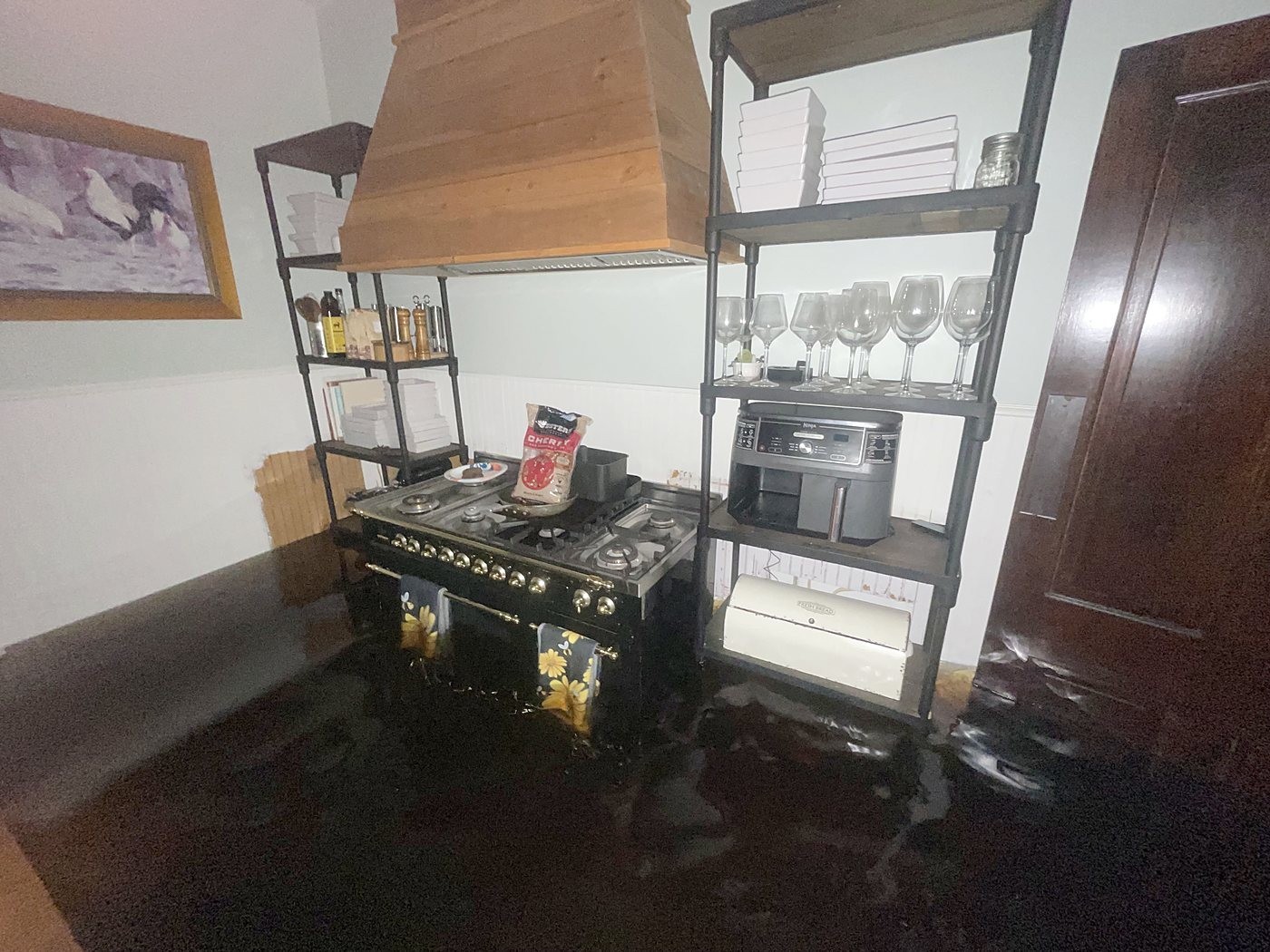 A kitchen with flood water standing across the floor, appliances and glassware still sitting on open shelving just above the water.
